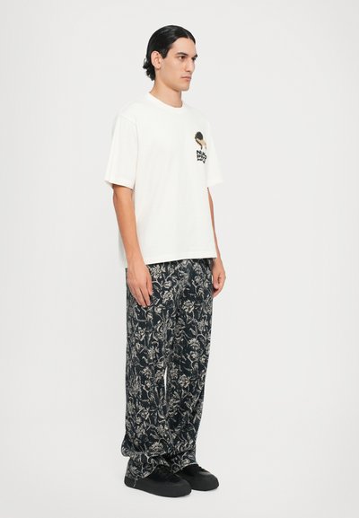 Tricou alb cu mânecă scurtă și imprimeu grafic, asortat cu pantaloni largi cu model floral în nuanțe de navy. Încălțămintea neagră completează ținuta.