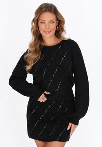 Schwarzes Strickoberteil und Rockset mit einem strukturierten Muster und diagonalen metallischen Akzenten. Lange Ärmel, gerippte Bündchen und Saum.