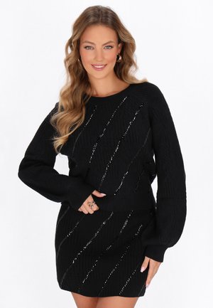 Set composto da maglione e gonna neri a maglia, caratterizzato da un motivo testurizzato con accenti metallici diagonali. Maniche lunghe, polsini a coste e orlo.