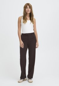 Pantalon marron ajusté avec une coupe droite, taille haute et poches latérales, associé à un débardeur blanc et des baskets.