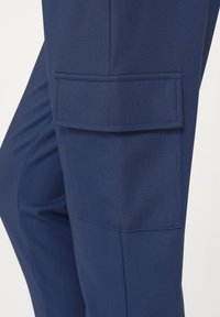 Navy blue cargo pants featuring a large side pocket, smooth texture, and structured design. Reinforced stitching along the seams.