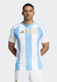 Argentinas landslagströja i vitt och ljusblå ränder, med en gyllene FIFA-emblem och AFA-symbol, tillverkad av fukttransporterande tyg.