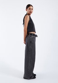 Black denim cropped tank top with a ribbed texture, paired with high-waisted, wide-leg black jeans and a black belt.