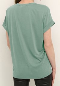 Krátký rukáv, volně střižené tričko z jemné, světle zelené látky. Obsahuje ohrnuté rukávy a kulatý výstřih, s hladkou, splývavou strukturou.