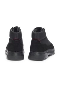 Zapatos altos negros de ante y textil con una suela de goma texturizada. Presentan un detalle en rojo y un diseño suave y curvado.