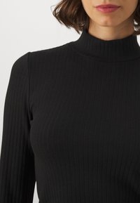 Svart ribbad polo tröja med långärmar och en tight passform, tillverkad av ett strukturerat stickat tyg med vertikala ränder.