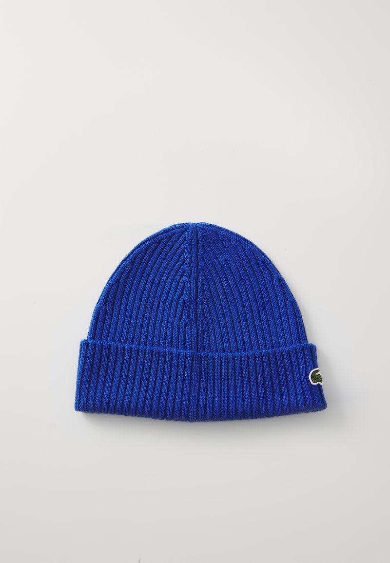 Blå ribbestrikket lue med brettet opp kant og en liten grønn brodert logo på siden. Myk tekstur og tettsittende design.
