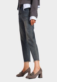 Jeans blu sbiaditi con orlo frangiato abbinati a scarpe con tacco alto in pelle marrone dotate di una fibbia decorativa.