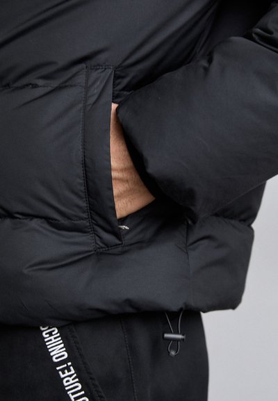 Sort pufferjakkeærme med en sidelomme, der har en glat tekstur og detalje med snøre til justerbar pasform.