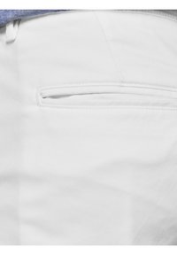 Poche de pantalon blanche avec une fine fente horizontale et une partie d’une chemise bleue visible au bord supérieur.