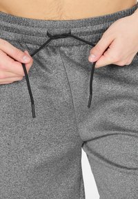 Grijze sweatpants met een gestructureerde afwerking, voorzien van een zwarte koord aan de taille en een ontspannen pasvorm. Close-up van de tailleband en het koord.
