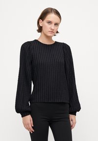 Black ribbed pullover with long puff sleeves, textured fabric, round neck, and a relaxed fit. Worn with slim black pants for contrast.