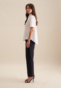 Camicia bianca a maniche corte con colletto, abbinata a pantaloni blu navy a vita alta e sandali neri con tacco, caratterizzata da una vestibilità comoda e un design moderno.