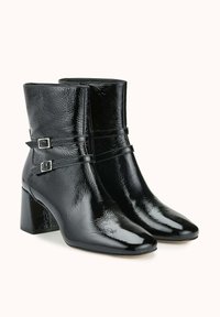 Bottines en cuir verni noir avec bouts pointus, talons blocs et détails à double boucle autour de la cheville.