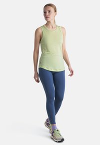 Top sin mangas de color verde claro con una textura suave, combinado con legging azules y zapatillas deportivas de tonos neutros.