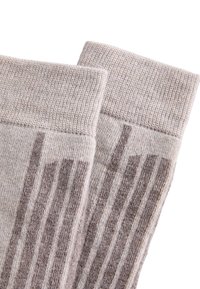 Ett par beige ribbad stickade strumpor med vikta muddar, visade nära på en vit bakgrund.