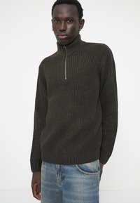 Dark brown, textured sweater with a high collar and a silver zip. Paired with light blue jeans showing a faded design.