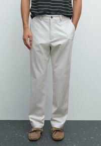 Chinos beige chiaro con un design a gamba dritta, dotati di chiusura con bottone e zip, tasche laterali e tessuto testurizzato. Abbinati a mocassini marroni.