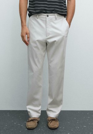 Helle beige Chinos mit geradem Bein, ausgestattet mit einem Knopf- und Reißverschluss, Seitentaschen und strukturiertem Stoff. Kombiniert mit braunen Mokassins.