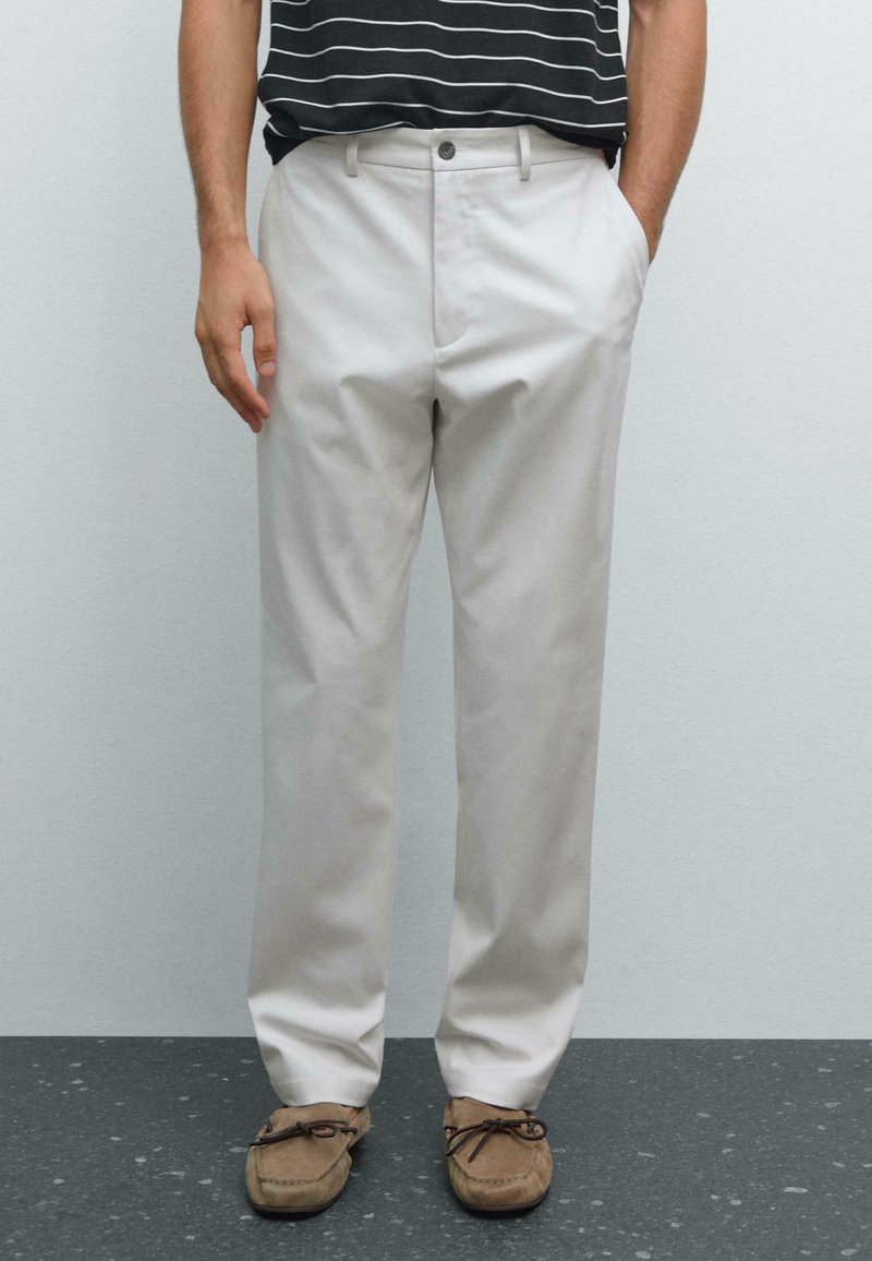 Chinos beige chiaro con un design a gamba dritta, dotati di chiusura con bottone e zip, tasche laterali e tessuto testurizzato. Abbinati a mocassini marroni.