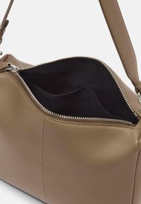 Brązowa skórzana torebka na ramię z zamkiem błyskawicznym w kolorze srebrnym, z przestronnym czarnym wnętrzem oraz zarysowaną, ale elastyczną konstrukcją.