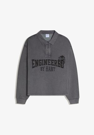 Tummanharmaa pitkähiha polo-paita, jossa kaulus, kaksi nappia ja rinnassa painettu "Engineered by Habit" -teksti sekä vaakuna.