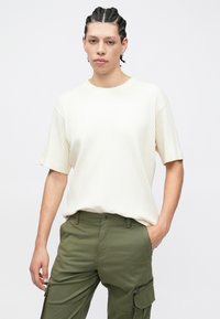 Κρεμ κοντομάνικη μπλούζα με ρίγες και στρογγυλή λαιμόκοψη, συνδυασμένη με χακί cargo παντελόνι με πλαϊνές τσέπες και φερμουάρ.