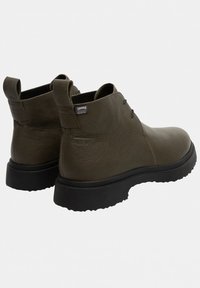 Olivgrønne læder ankelstøvler med sorte tykke gummisåler, trækklapper og et lille Camper GORE-TEX mærke på siden.