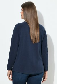 Camiseta de manga larga azul marino con un ajuste relajado y mangas raglán. Textura suave, dobladillo curvado y un sutil patrón jaspeado. Combinada con jeans oscuros.