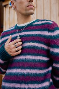 Multicolored striped sweater in pink, purple, and teal, made of fuzzy fabric. Features ribbed cuffs and an embroidered text detail.