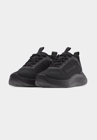 Paire de baskets noires Calvin Klein avec semelles épaisses, lacets à l'avant, et languettes à la languette et au talon.