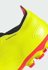 Botín de fútbol amarillo brillante con parte superior texturizada, acentos en negro y suela rosa. Presenta la marca "HYBRIDFEEL" en el lado lateral.