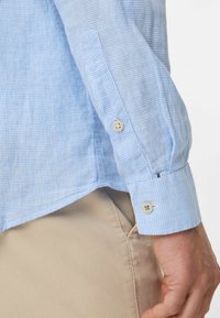 Camicia a quadri blu chiaro con polsino abbottonato, realizzata in un tessuto dalla consistenza morbida. Il polsino presenta un dettaglio con un singolo bottone.