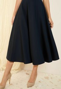 Navy A-line dress with a flared hem and side seam details, paired with beige pointed-toe heels on a textured surface.