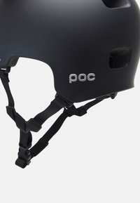 Casco nero con finitura opaca, dotato di fori di ventilazione, cinturini neri regolabili e un logo argento sul lato. Ideale per dispositivi di sicurezza.