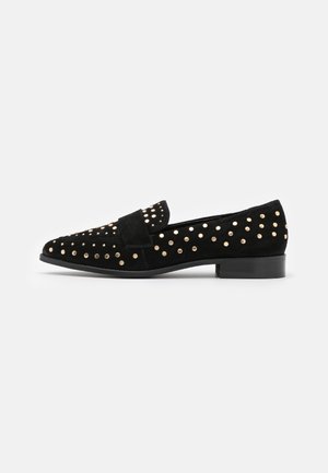 Mocassin en daim noir avec de petits clous dorés couvrant la tige et un petit talon carré, présenté de côté sur fond blanc.