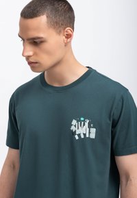 Donkerblauwe katoenen t-shirt met korte mouwen, voorzien van een grafisch ontwerp van verschillende vormen en kleuren op de linkerborst.