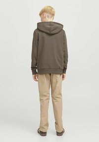Felpa con cappuccio marrone e tasca a marsupio, abbinata a pantaloni beige e sandali marroni, vista da dietro. Design semplice e casual.