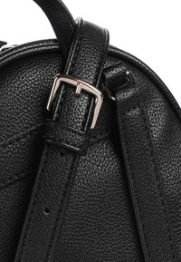 Détail d'un sac en cuir noir avec une surface texturée, une bandoulière réglable avec une boucle métallique, et des accents de couture.