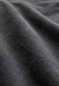 Tissu gris texturé avec un motif côtelé subtil, présentant des plis doux et une surface lisse. La perspective en gros plan met en valeur les détails du matériau.