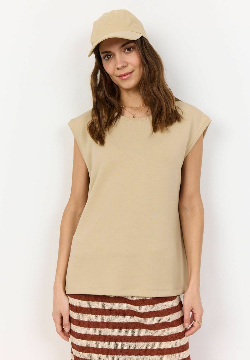 Beige sleeveless top made of soft fabric, featuring a round neckline. Paired with a khaki cap and a striped knitted skirt in brown and cream.