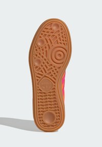 Rubber shoe sole in orange with textured patterns, including circular and linear designs, and an embossed logo at the heel.