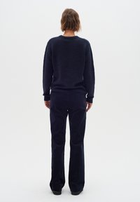 Tume sinine sviiter struktuurse viimistlusega, pikkade varrukatega ja ümar kaelus; koos vastavate tumesiniste laiade pükstega.