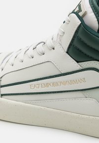 Höga sneakers i vitt läder med gröna detaljer. Har en texturerad häl, kontrasterande ränder och ett prägla varumärkeslogotyp i guld.