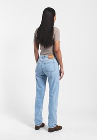 Jeans de denim azul claro con un corte recto, que presentan una etiqueta marrón en la parte trasera de la cintura y una superficie suave y ligeramente texturizada.
