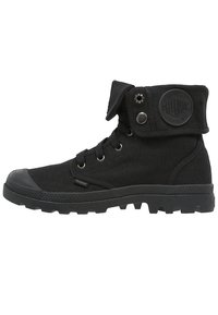 Bottines cheville en toile noire avec une semelle en caoutchouc, œillets en métal, et un revers pliable avec un patch logo et un détail de bouton-pression.