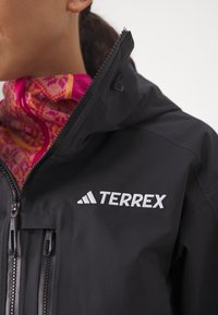Schwarze, wasserdichte Jacke mit Kapuze, Reißverschlusstaschen und gesticktem "TERREX"-Logo. Die innere Schicht hat einen kragen mit pink-und orangefarbenem Muster.