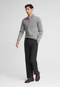 Grauer Reißverschluss-Pullover mit langen Ärmeln, kombiniert mit dunklen Hosen und braunen Schuhen. Das Outfit hat ein strukturiertes Design und eine lässige Passform.