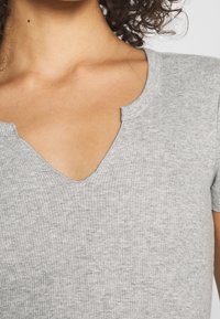 Grå ribbet kortærmet top med V-udskæring og rå kantfinish. Blød tekstur med et tætsiddende design, der fremhæver enkle, rene linjer.