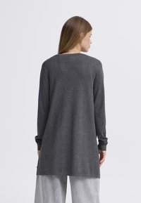 Sivo pulover z dolgimi rokavi s preprostim, ravnim krojem, rebrastim izrezom in rahlo daljšim zadnjim delom. Mehka tekstura, minimalističen dizajn, brez vidnih vzorcev.
